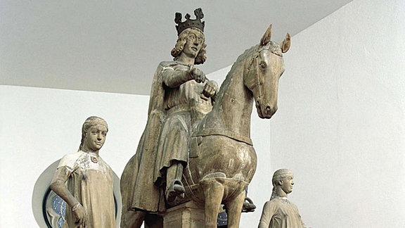 Statue eines Mannes mit Krone auf einem Pferd, rechts und links daneben jeweils eine Frauengestalt