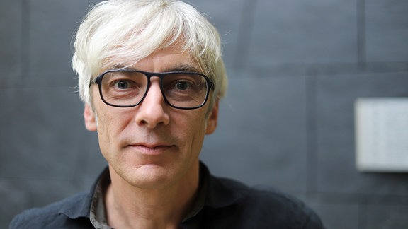 Portraitfoto Stefan Kanis. Ein Mann mit Brille und kurzem hellblondem Haar schaut in die Kamera. 