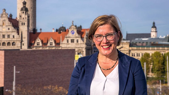 Skadi Jennicke, eine Frau mit kinnlangen blonden Haaren, Brille, weißer Bluse und blauem Sakko, steht auf einem Balkon