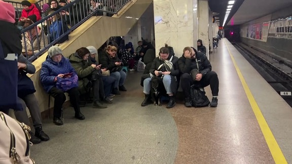 Menschen sitzen an einer U-Bahnhaltestelle.