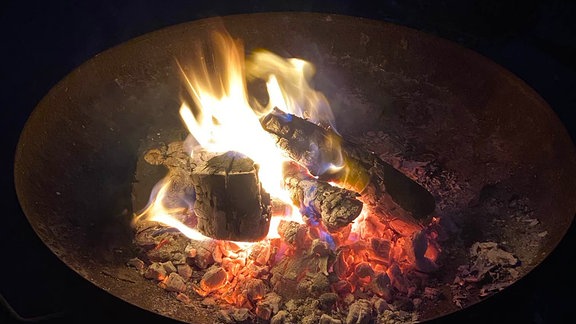 Eine Feuerschale im Garten mit Holzscheiten, die brennen.