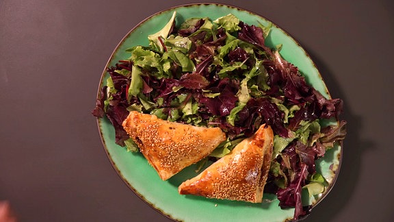 Blätterteigtaschen, Salat und Gemüse liegen auf einem Teller.