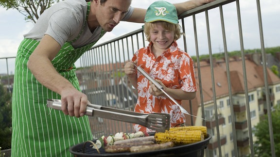 Ein Vater grillt mit seinem kleinen Sohn auf dem Balkon .