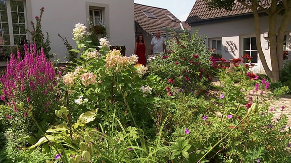 Blühendes Staudenbeet, dahinter zwei Personen