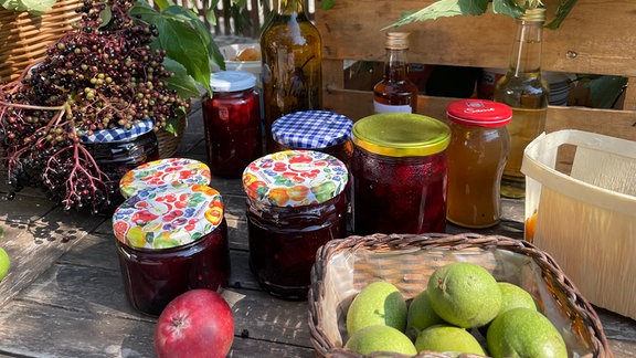 Ernte im Herbst: Zierquitten, Holunderbeeren, Marmeladengläser, grüne Walnüsse und andere Wildfrüchte liegen auf einem Tisch.