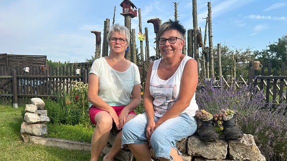 Zwei Frauen sitzen auf einer Naturstein-Mauer.