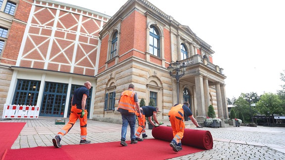 Arbeiter befestigen den roten Teppich für die Eröffnung der Bayreuther Richard-Wagner-Festspiele vor dem Festspielhaus auf dem Grünen Hügel.