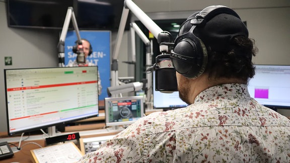 Zwei Männer mit Hemd und Fliege stehen an Mikrofonen in einem Radio-Studio