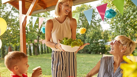 Glückliche Frau serviert Salat auf einer Gartenparty.