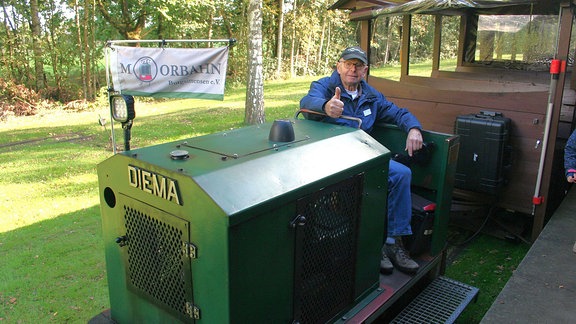 Ein Mann sitzt auf einer kleinen grünen Eisenbahn, der Moorbahn.