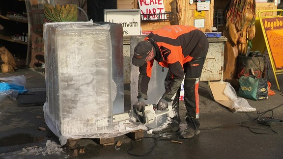 Mann zersägt mit Kettensäge einen Eisblock