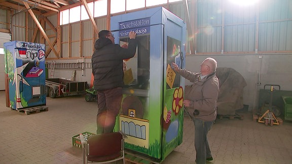 Zwei Männer gestalten eine bunte Telefonzelle