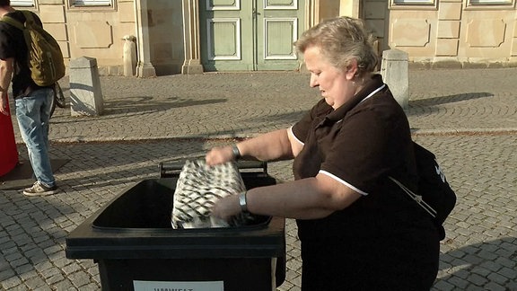 Eine Frau entleert einen Beutel in eine Mülltonne.