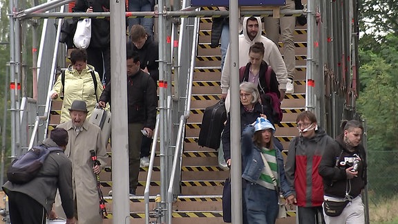 Bahnpassagier*innen benutzen eine provisorische Brücke.