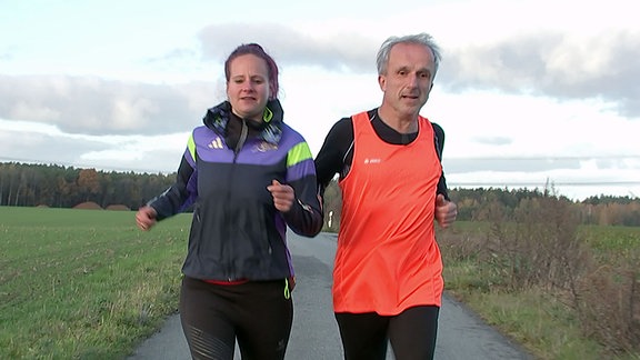 Eine Frau geleitet einen blinden Mann beim Lauftraining