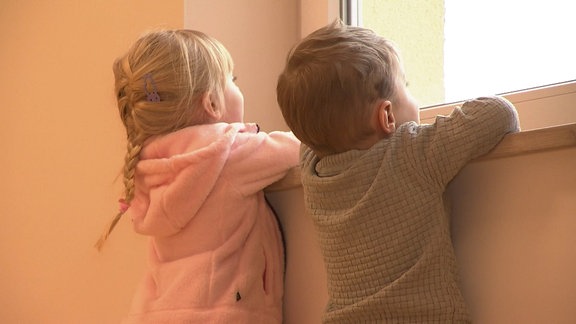 Zwei Kinder schauen aus einem Fenster.