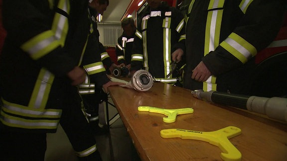 Auf einem Tisch zwischen Feuerwehrleuten liegen zwei gelbe Plastikteile.