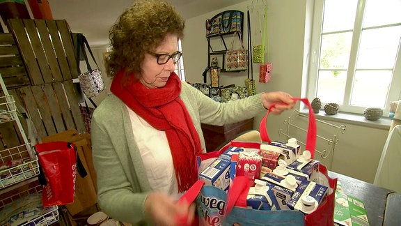 Eine Frau zeigt eine große Tasche voller alter Verpackungen.