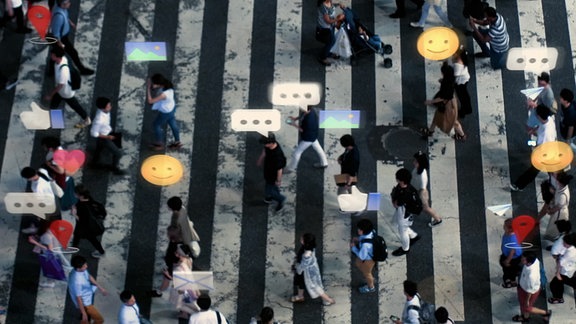 Blick von oben auf eine belebte Straße: Über einen Zebrastreifen laufen zahlreiche Fußgänger über deren Köpfe Emojis, Textblasen, Like-Symbole und Herzen auftauchen.