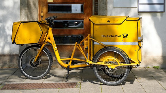 Ein gelbes Postfahrrad der Deutschen Post steht vor einer Haustür