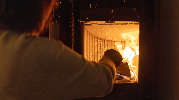 Frau legt in einem Kamin Holz nach.