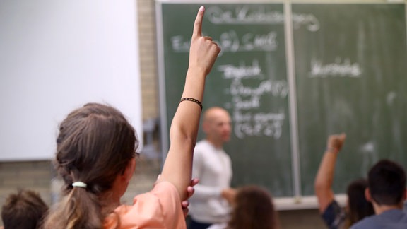 Eine Schülerin der fünften Klass hebt im Unterricht den Finger. 