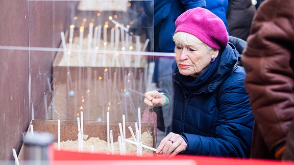 Eine Frau zündet anlässlich von 35 Jahre friedliche Revolution und Mauerfall am Denkmal der Gedenkstätte Berliner Mauer eine Kerze an