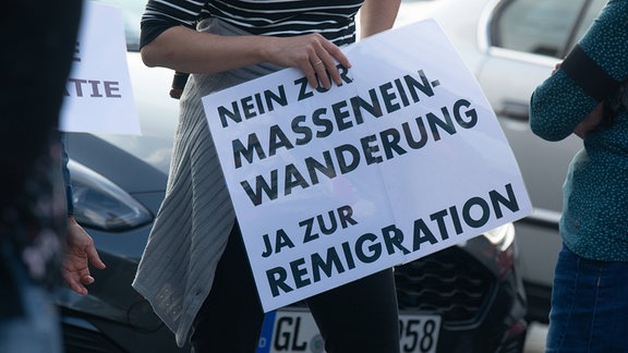 Demonstrantin hält Schild mit Schriftzug "Nein zur Masseneinwanderung / Ja zur Remigration"