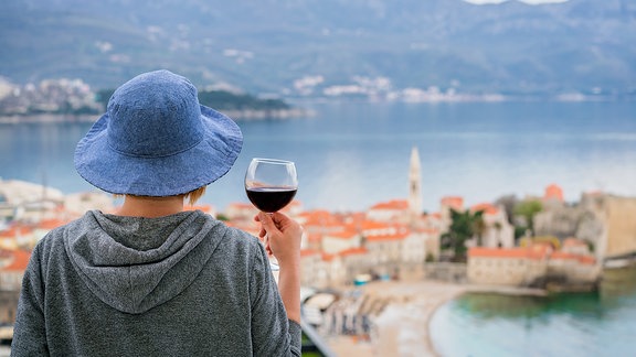 Eine Frau von hinten mit einem Glas Rotwein