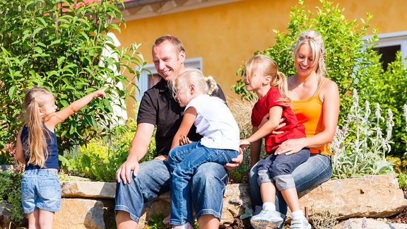 Eine Familie sitz freudig vor einem Eigenheim.