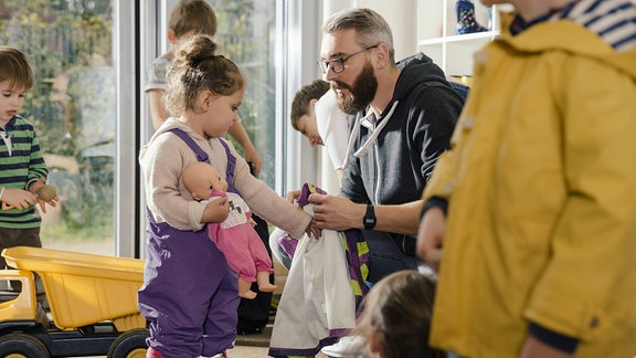 Vorschullehrer hilft Kind beim Anziehen.