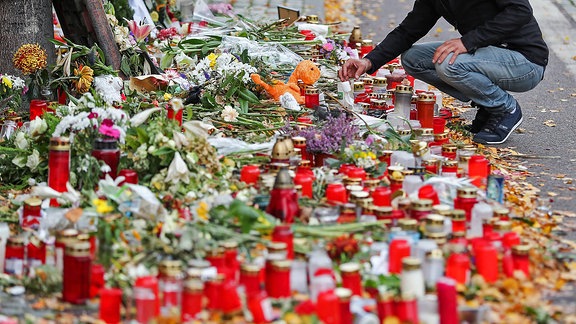 Ein Mann hockt vor dem Meer aus Kerzen und Blumen vor einem Imbiss