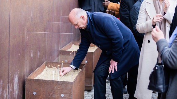 Kai Wegner (CDU), Regierender Bürgermeister von Berlin, zündet bei der zentralen Gedenkveranstaltung anlässlich von 35 Jahre friedliche Revolution und Mauerfall am Denkmal der Gedenkstätte Berliner Mauer eine Kerze an.