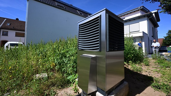 Vor einem neu gebauten Wohngebäude ist im Garten eine Wärmepumpe zum Heizen des Gebäudes in Betrieb.