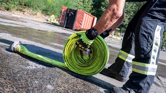 Ein Mitarbeiter der Feuerwehr rollt einen Feuerwehrschlauch zusammen