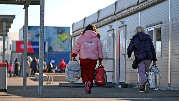 Mit Gepäck gehen zwei Frauen durch eine Aufnahmeeinrichtung für Geflüchtete aus der Ukraine in Leipzig.