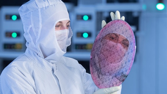 Eine Frau in Schutzkleidung hält in einem Automatisierungslabor einen Test-Wafer