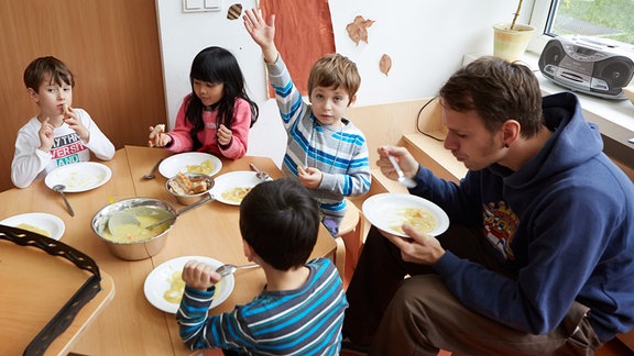 Vorschulkinder und ihr Erzieher beim Mittagessen in der Kita