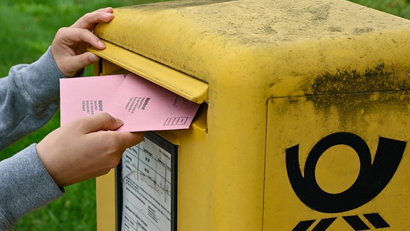 Eine Person wirft 2021 zwei Briefwahlunterlagen in einen Postkasten der Deutschen Post.