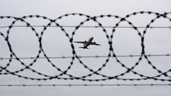 Abschiebung: Ein Flugzeug von Lufthansa startet am Flughafen Hannover - fotografiert durch Stacheldraht am Flughafenzaun.