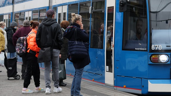 Fahrgäste stehen vor einer einfahrenden Straßenbahn.