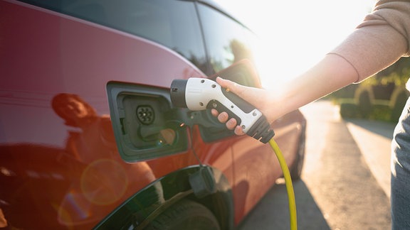 Frau schließt Elektro-Auto an Ladestation an.