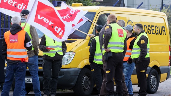 Teilnehmer eines Streiks stehen vor einer Niederlassung von Prosegur in Hamburg an einem Geldtransporter.