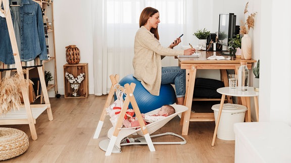 Eine Frau mit Smartphone sitzt an einem Arbeitsplatz.