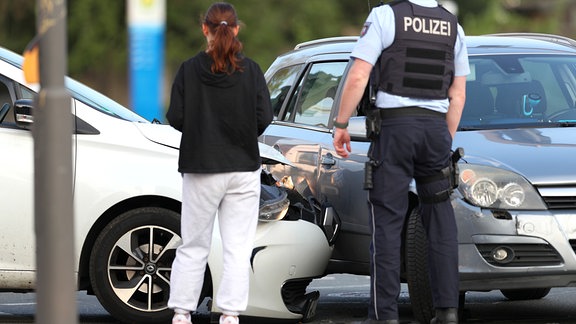 Symbolbild: Eine Frau und ein Polizist vor zwei PKW, die ineinander gefahren sind.