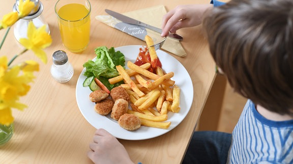 Ein Junge sitzt vor einem Teller mit Chicken Nuggets und Pommes Frites 