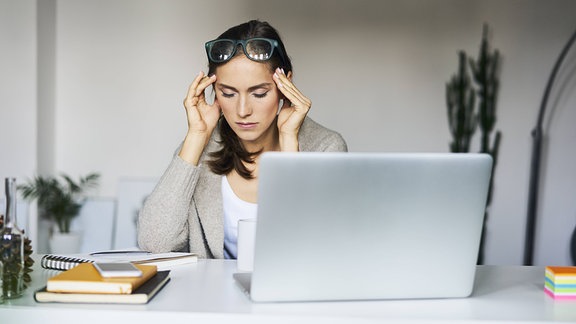 Eine Frau an einem Laptop reibt sich die Schläfen