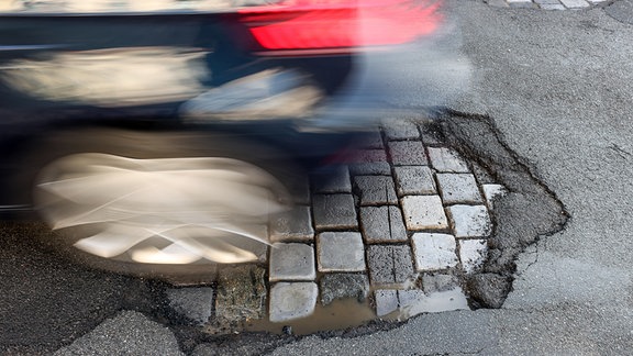 Ein Auto fährt über eine Straße mit Schlaglöchern. 