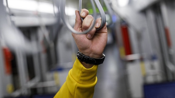 Ein Fahrgast in der Straßenbahn hält sich an einer Halteschlaufe fest.