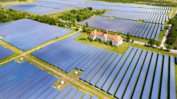 Vogelperspektive auf Solarmodule, die rings um ein altes, herrschaftliches Gebäude stehen